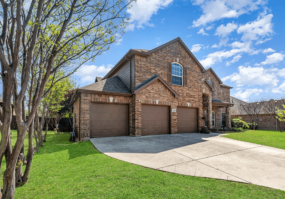A brick house with three garage doors under a blue sky.